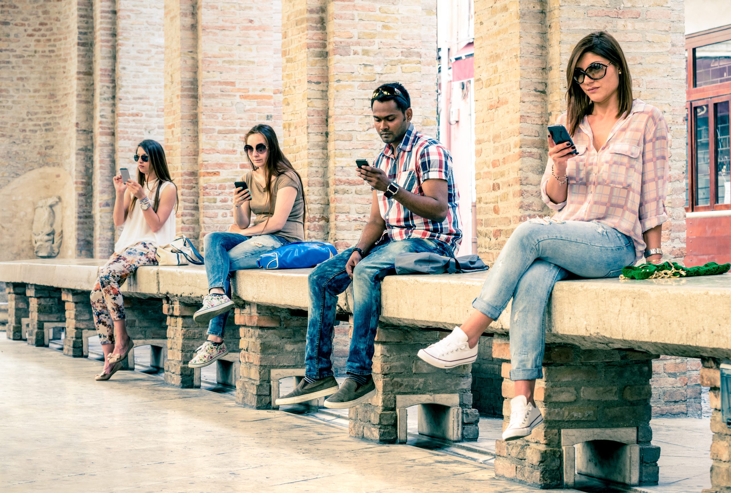 Group of young multiracial friends using smartphone with mutual disinterest towards each other - Technology addiction in actual lifestyle - Soft vintage filtered look with main focus on male person